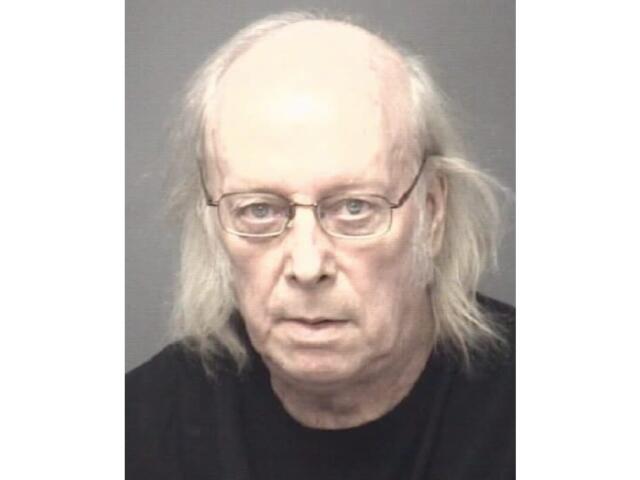 Mugshot of an older man with thin glasses, balding head and shoulder‑length gray hair, wearing a black shirt.