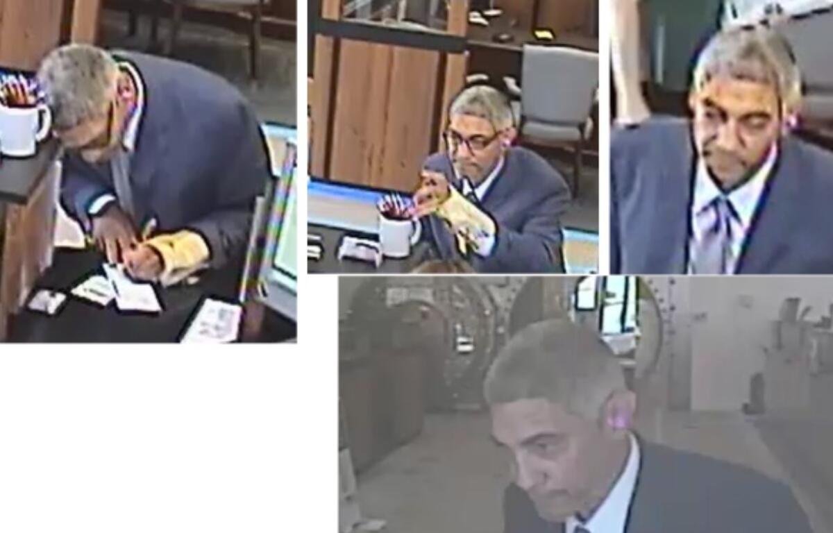 Man in a suit signs documents at a desk with a coffee mug and papers nearby in what looks like a service counter area inside a building.