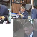 Man in a suit signs documents at a desk with a coffee mug and papers nearby in what looks like a service counter area inside a building.