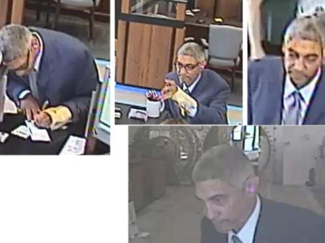 Man in a suit signs documents at a desk with a coffee mug and papers nearby in what looks like a service counter area inside a building.