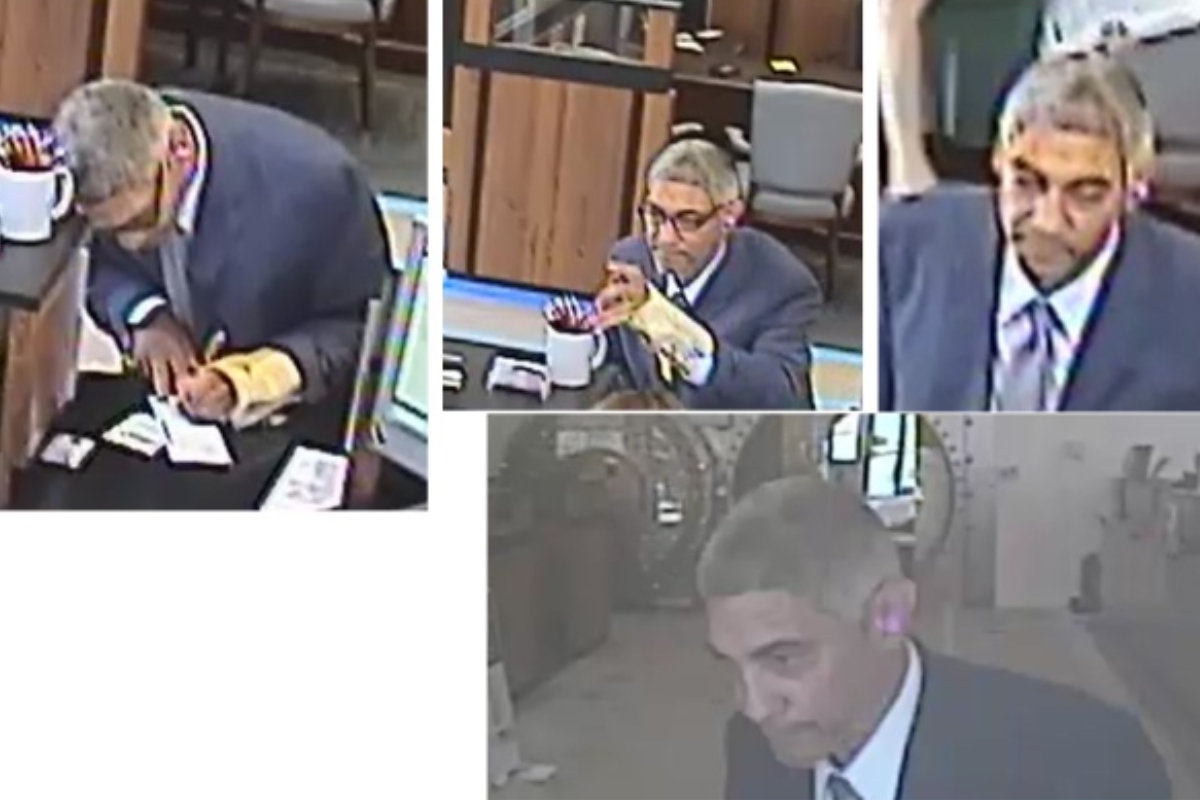 Man in a suit signs documents at a desk with a coffee mug and papers nearby in what looks like a service counter area inside a building.