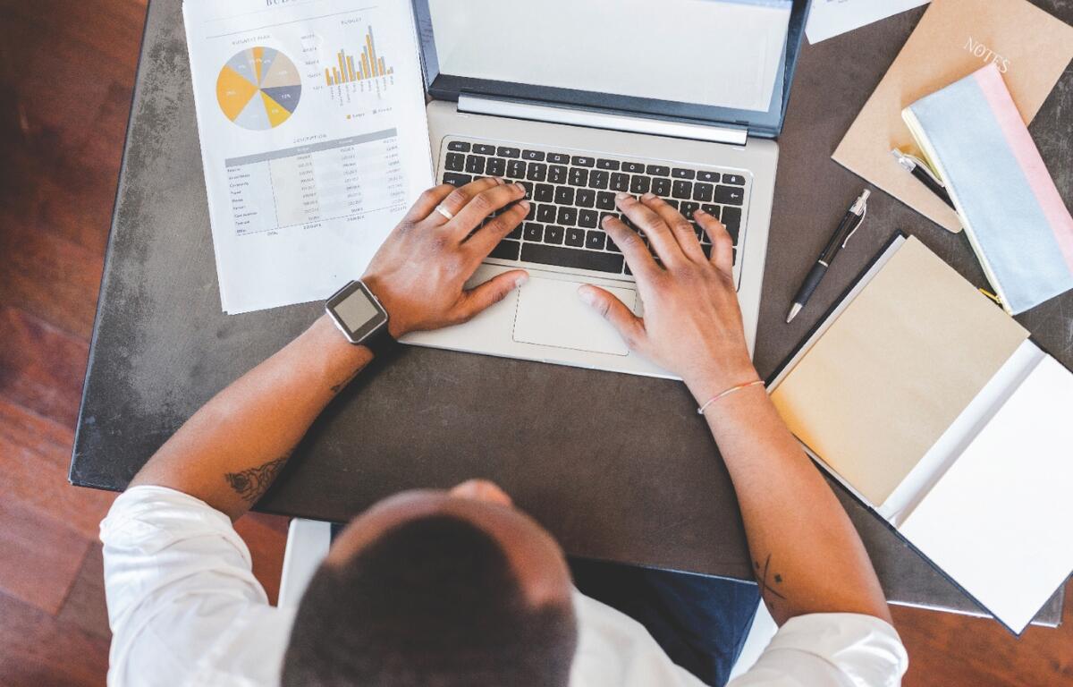 A man sitting at a laptop with papers around it.
