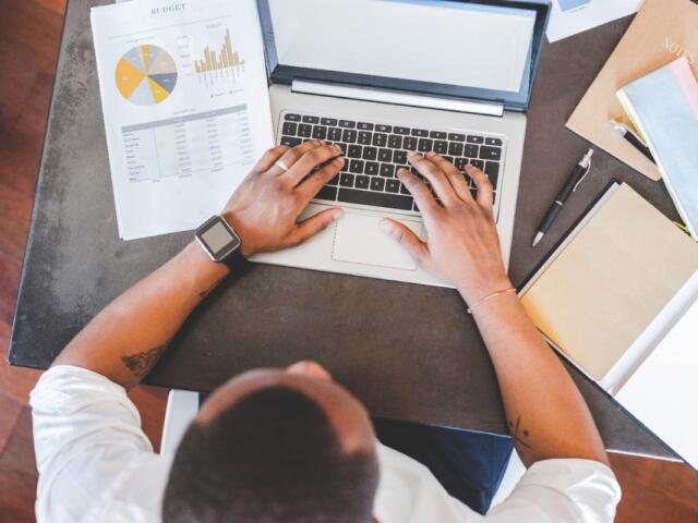 A man sitting at a laptop with papers around it.