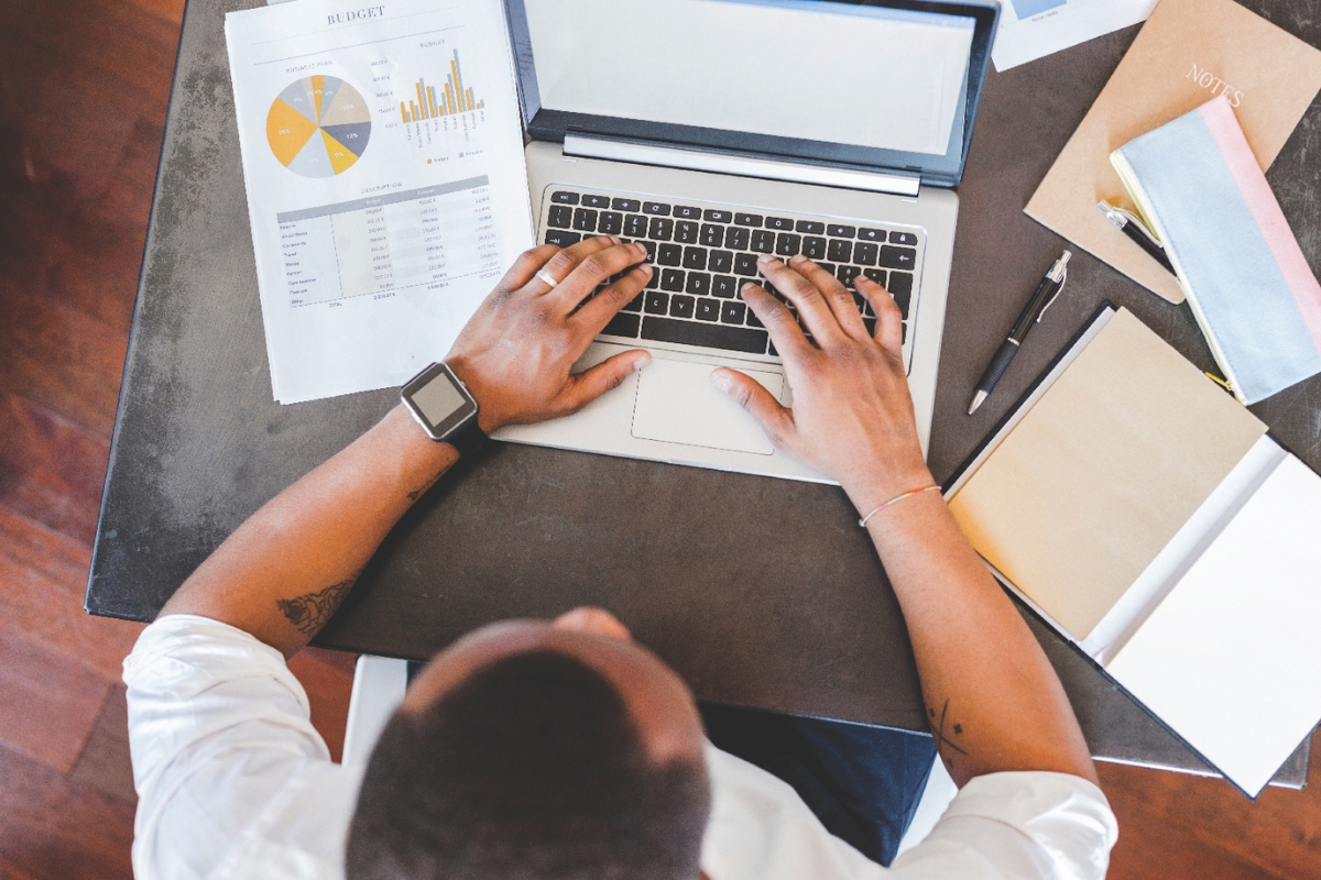 A man sitting at a laptop with papers around it.