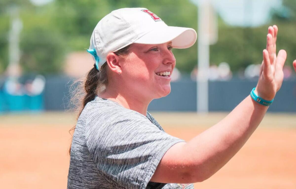 Smiling woman in a white cap and gray shirt gives a high-five on a baseball/softball field.