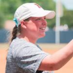 Smiling woman in a white cap and gray shirt gives a high-five on a baseball/softball field.