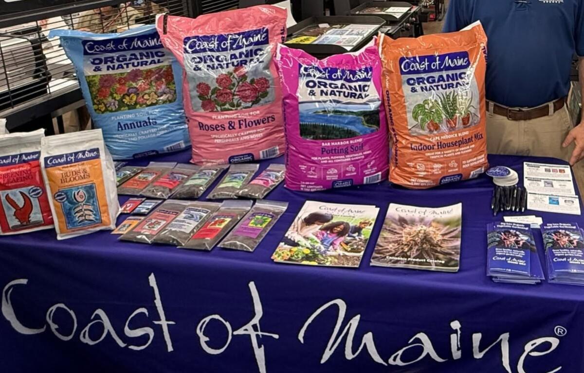 Coast of Maine gardening display with organic soil bags on a blue tablecloth, plus brochures and seed packets nearby.