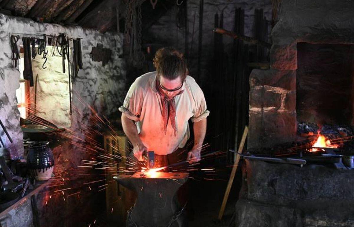 Blacksmith at an anvil, shaping glowing metal with sparks flying in a dim, workshop-style forge.
