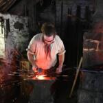 Blacksmith at an anvil, shaping glowing metal with sparks flying in a dim, workshop-style forge.