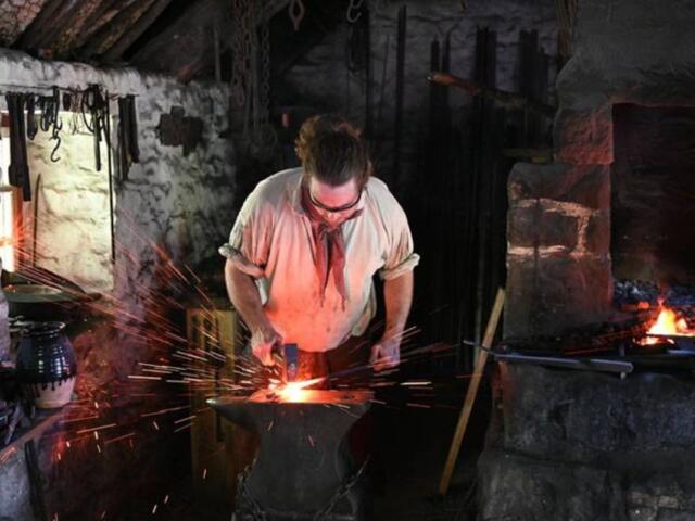 Blacksmith at an anvil, shaping glowing metal with sparks flying in a dim, workshop-style forge.