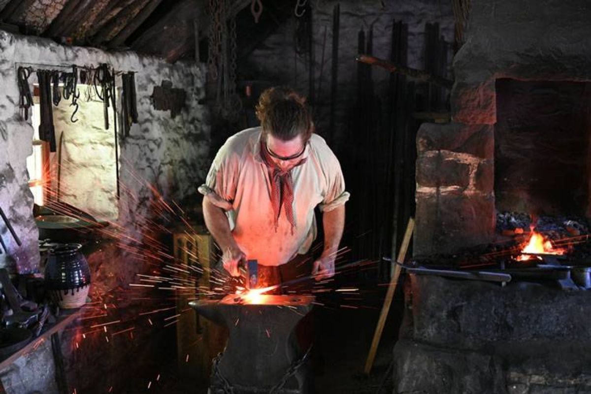 Blacksmith at an anvil, shaping glowing metal with sparks flying in a dim, workshop-style forge.